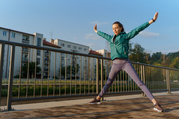 Fototapeta na wymiar Attractive young woman stretching before her early morning run along the embankment of river.