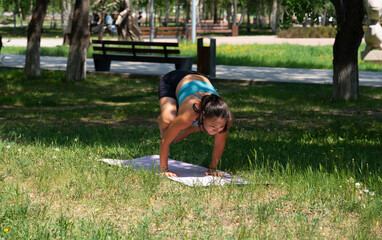 A young Asian (Kazakh) woman practices yoga in a city park in summer.