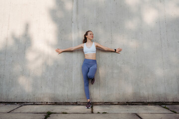 Fototapeta na wymiar Portrait of young sporty woman in sportswear excercising in front of concrete wall in the city.