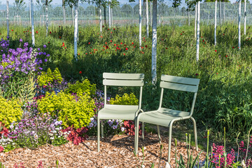 Two light green metal chairs in a lush blooming garden