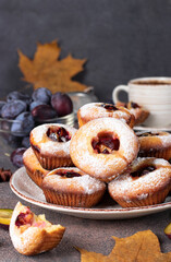Homemade muffins with plums sprinkled powdered sugar on plate and cup of coffee