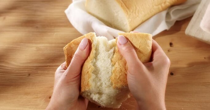 Female hands tear fresh bread. Texture of bread close up. Wooden background. Slow mation. Sunny day. First person view. 