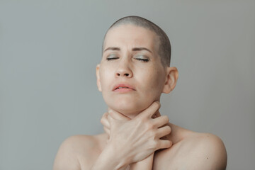  Portrait of an emotional young beautiful woman with a shaved head, she wrapped her arms around her neck and strangles herself. Denial of feelings. Result of chemotherapy