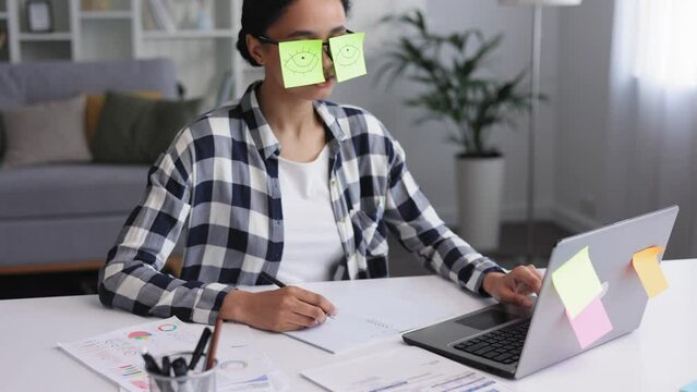 The concept of a lot of work. Tired african american female student sleeping with stickers on eyes while sitting at desk. A woman pretends to work in the office, although she is asleep.