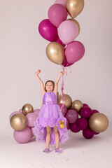 Fototapeta na wymiar Cute happy little girl in a lilac princess dress posing with air balloons isolated on white background. Kids Birthday party celebration concept. Happy Birthday banner with copy space. Studio shot.