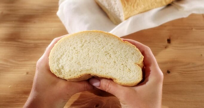 Female hands squeeze fresh bread. Check bread freshness. Wooden background. Slow mation. Sunny day. First person view. 