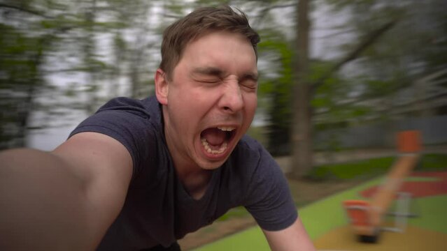 A young man is spinning on a carousel. A man has fun and shouts at the attraction close-up. First-person view.