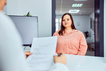 A plus-size brunette woman is sitting at the doctor's office, looking afraid.