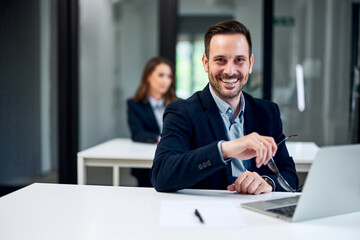 Portrait of a smiling businessman working over a laptop and holding his glasses.