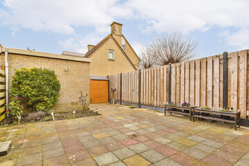 a backyard area with benches and wooden fenced in to the side of a house on a cloudy blue sky day