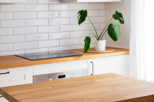 Wooden tabletop with free space for product montage or mockup against blurred white kitchen with cutting board and plant in scandinavian style