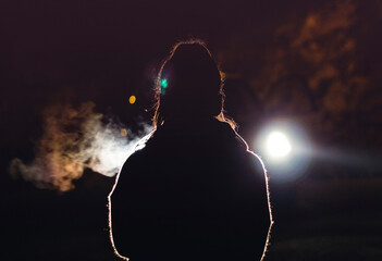 Chica de espaldas frente a la luz de un coche de noche y con frío - obrazy, fototapety, plakaty