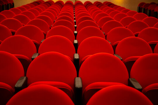 Algumas fileiras de poltronas na cor vermelha em um teatro vazio.