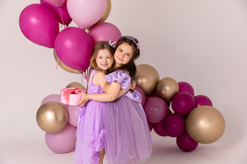 Fototapeta na wymiar Birthday celebration concept, little princess in lilac dresses, cheerful preschool girl party, two girls with balloons on the background, copy space