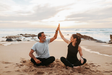 Glad mature european woman and man in sportswear practice yoga, give high five, enjoy workout together