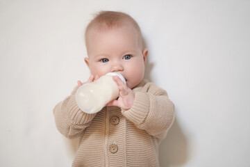 A newborn baby drinks milk from a bottle. Studio photo