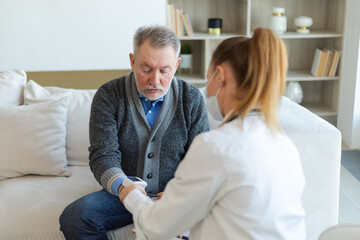 Female doctor senior man taking his blood pressure in doctor office or at home. Old man patient and doctor have consultation in hospital room. Medicine healthcare medical checkup. Visit to doctor