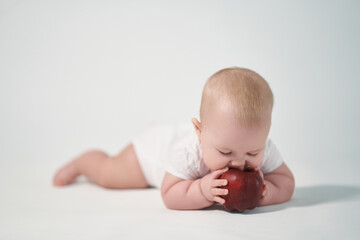 A 7 month old baby eats a red apple. photography on a white background