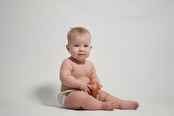 a child of 7 months sitting on the pope holds a red apple in his hands. photography on a light...