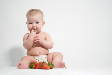 A six-month-old baby eats red strawberries, takes pictures on a light background