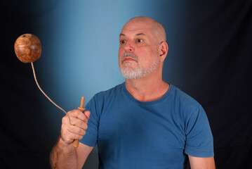 happy bald man with white beard playing with antique children's toy bilboquet looking forward with...