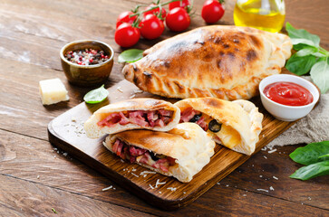 Delicious Pizza Calzone, Italian Pizza Stuffed with Ham and Cheese with Tomatoes and Fresh Basil on...