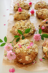  Delicious sweet rolls with crumble on a light background, homemade pastries in a rustic style with pink roses decoration, food concept, close-up.