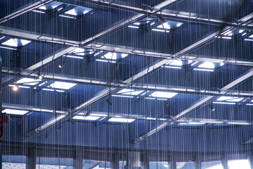 Fragment of light-transmitting ceiling with built-in windows in industrial, public or administrative building. Ceiling of square cells through vertical filamentous transparent blinds.