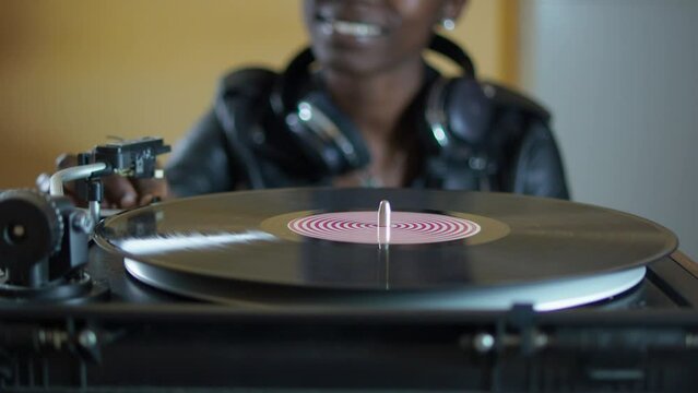young woman wearing a leather jacket using headphones while playing a vinyl record on a vintage turntable