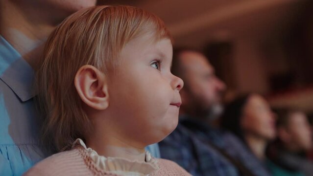 Cute little girl watching a performance in theatre or movie in cinema. Leisure entertainment for family with kids. Cultural event for children.
