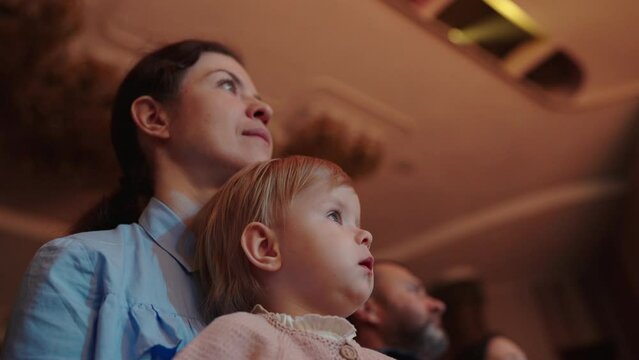 Cute little girl with her mother watching a performance in the theater or movie in the cinema. Leisure entertainment for family with kids. Cultural event for children.