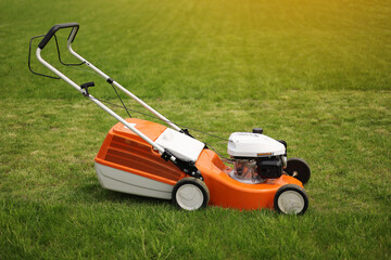 Top view of modern orange-grey electric lawn mower cutting bright lush green grass. Gardening work tools. Rotary lawn mower machine on lawn. Professional lawn care service. Place for text.
