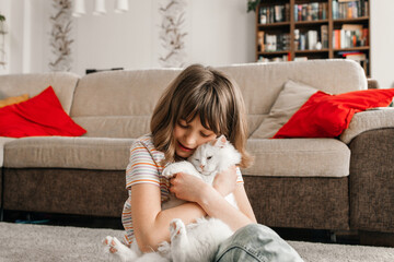 A teenage girl sits on the floor in the living room and plays with her beloved kitten. The child...