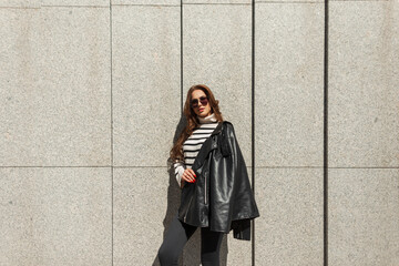 Fashionable beautiful young hipster girl with sunglasses in stylish urban rock clothes with leather...