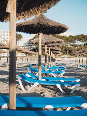 Blue sunbeds and straw umbrellas on a touristic beach