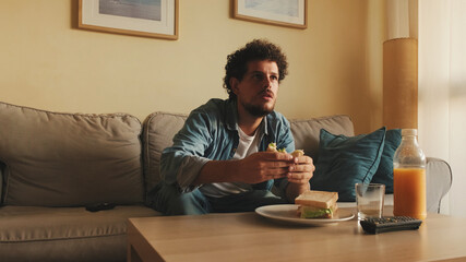 Guy dressed in denim shirt has lunch, sits in the living room and emotionally watches sports game on TV