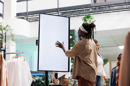 Customer interacting with digital smart board in clothing retail store. African american man tapping on whiteboard blank screen to read information about shoes new collection in shopping mall