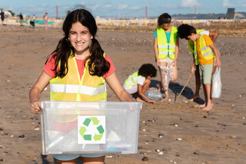 Smiling teen arab girl carries box for recycling, multiethnic children volunteers in vests collect...