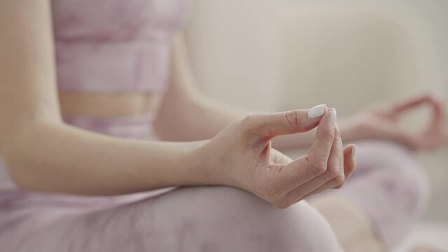 Close-up woman sitting in lotus position and meditating, practicing yoga at home. View of the fingers. Calm girl controlling emotions. Slow motion