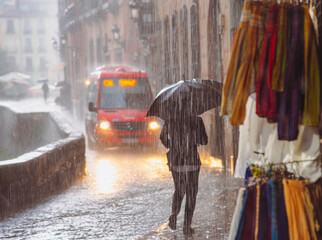 Figures scurrying along the old streets of an European city, seeking shelter from the rain under...