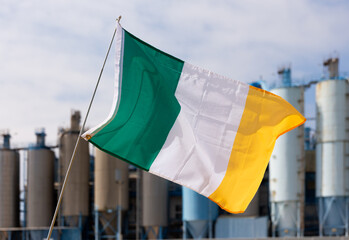 Irish flag flies proudly in wind in front of factory
