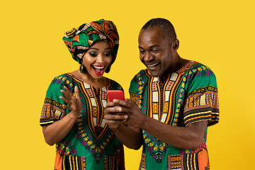 Emotional black couple checking content on cell phone, yellow background