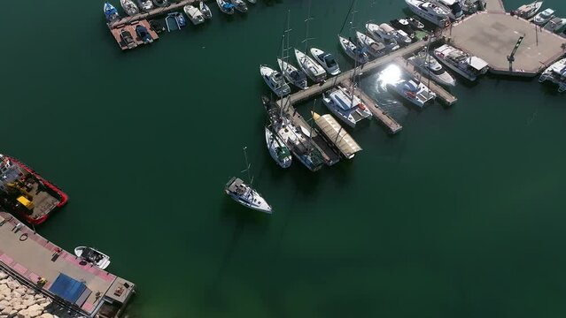 Aerial view of a Small sail boat leaving a marina slowly 