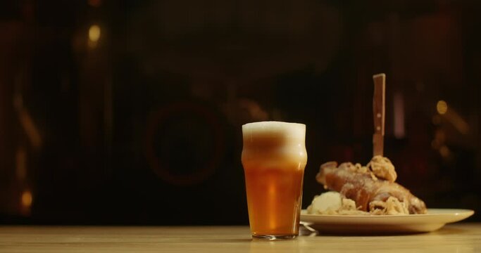 Glass of beer on bar counter. Jugs, mugs, pints of brew beverage, ale, cider on wooden table in pub, bar. Appetizer of meat shank with mashed potatoes