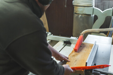 Carpenter sliding wooden plank under table saw to cut wood in woodworking studio. High quality photo