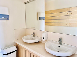 double sink in small public toilet with wall soap dispenser and paper towlels