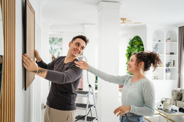 man and woman caucasian couple hanging painting on the wall at home