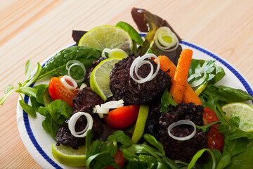 Dish of blood sausage with different greens, tomatoes and lemon served at plate
