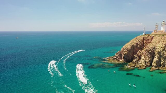 Aerial view of boats sailing along the Faro de Cabo de Gata, a lighthouse along the wild coastline with cliffs, Almeria, Spain.
