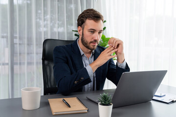 Businessman in black suit working on laptop at his workspace desk. Smart executive researching financial data and planning marketing strategy on corporate laptop at modern workplace. Entity
